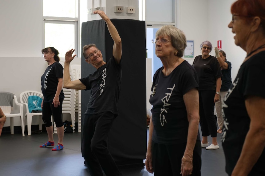 Dance studio rehearsal, Mr Butler standing in the centre with arms stretched above his head.