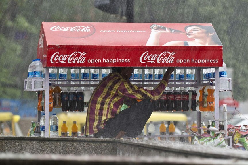 An Indian man takes shelter on his cold-drinks cart during a heavy downpour in New Delhi