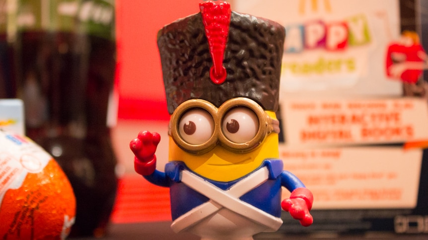 A child's toy sits next to a wrapped chocolate egg, in front of a fast food container.