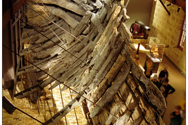 Worn timber planks displayed in the shape of a ship's hull.