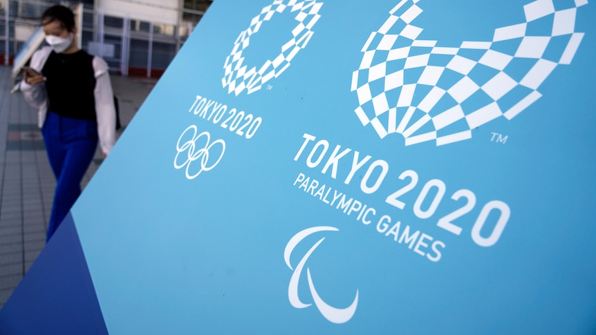 A woman walks near a blue sign of the Tokyo 2020 Olympic and Paralympic Games.
