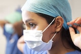 A doctor putting on blue protective gear.