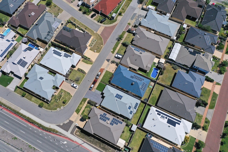 A suburb as seen from above, featuring many houses with solar panels on their roofs.