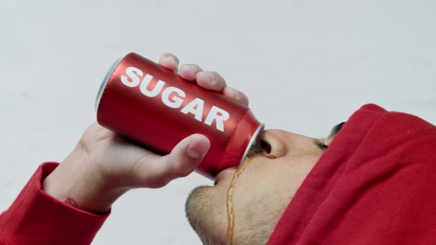 A man in a red hoodie drinks from a red can labelled 'sugar', with a cola-coloured liquid running down his cheek.