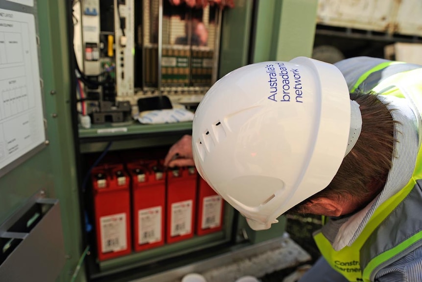 A man in a white hard hat fiddling with switches inside the node container.