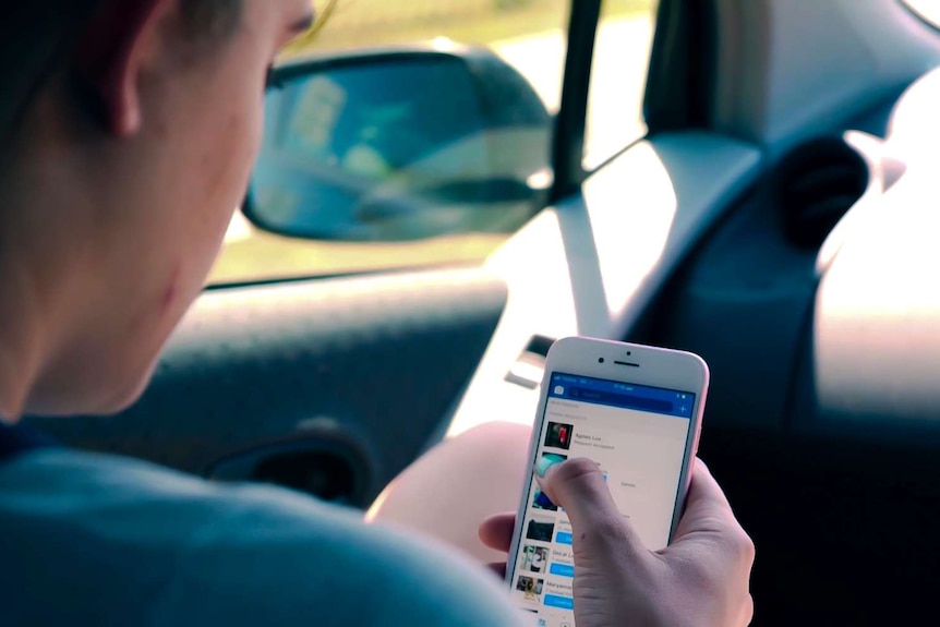 A woman holds her mobile phone while sitting in a car.