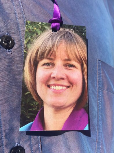 A photo of a smiling blonde woman is pinned to a blue button up shirt.