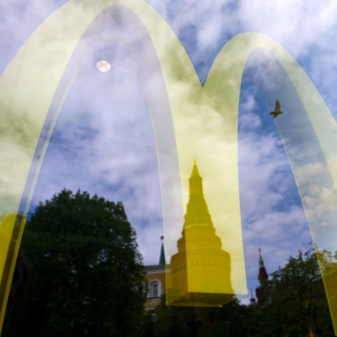 The Kremlin's towers are seen reflected in the window of a closed McDonald's restaurant in Moscow with a blue sky and a bird.