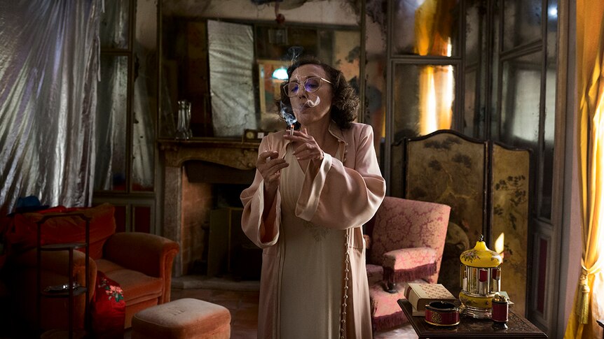 Colour still of Nicoletta Braschi standing and smoking in a rundown living room in 2018 film Happy as Lazzaro.