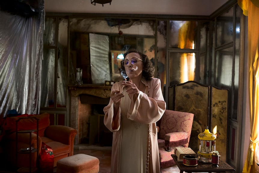 Colour still of Nicoletta Braschi standing and smoking in a rundown living room in 2018 film Happy as Lazzaro.