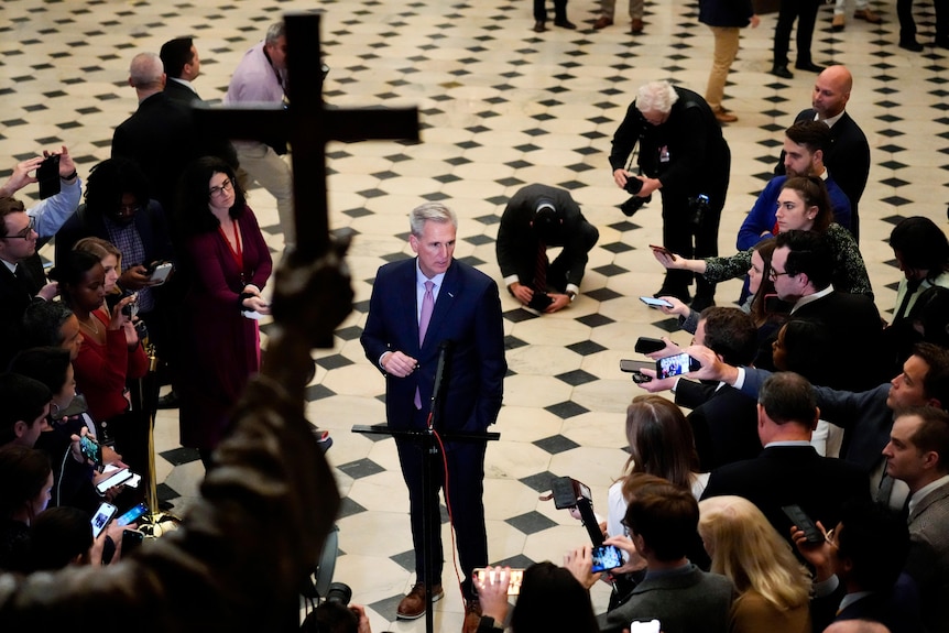 Kevin McCarthy stoi na marmurowej podłodze przed zestawem pras. 