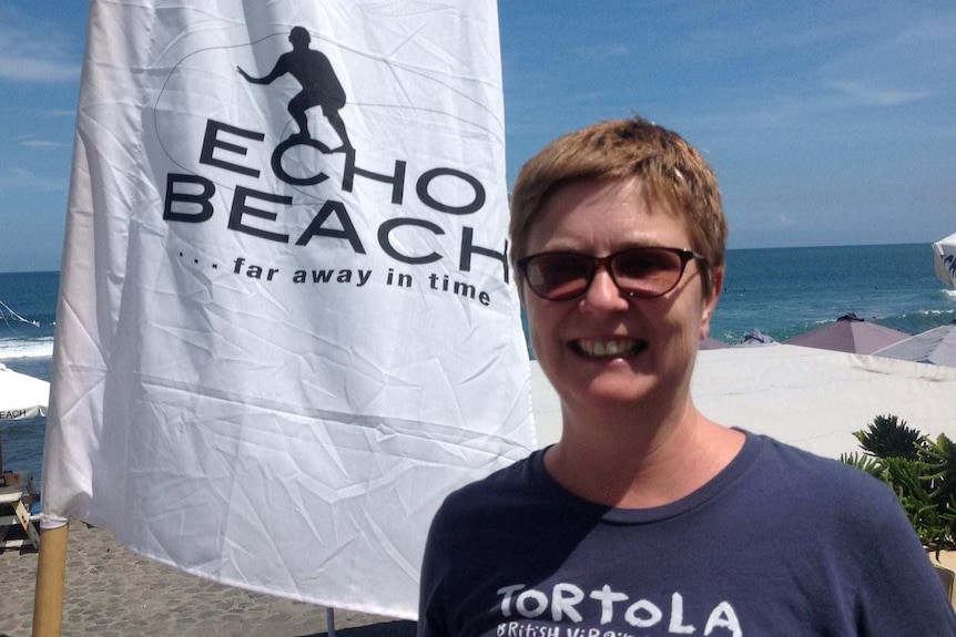 A woman smiles at a beach next to a flag that says Echo beach.