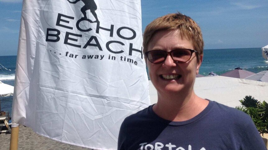 A woman smiles at a beach next to a flag that says Echo beach.