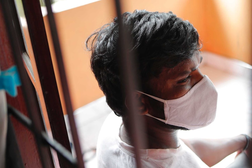 A Sri Lankan man in a face mask  shot through a window
