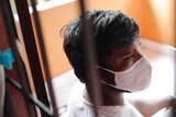 A Sri Lankan man in a face mask  shot through a window