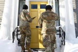 National guard members check on residents, in army fatigues knocking on a yellow door in winter