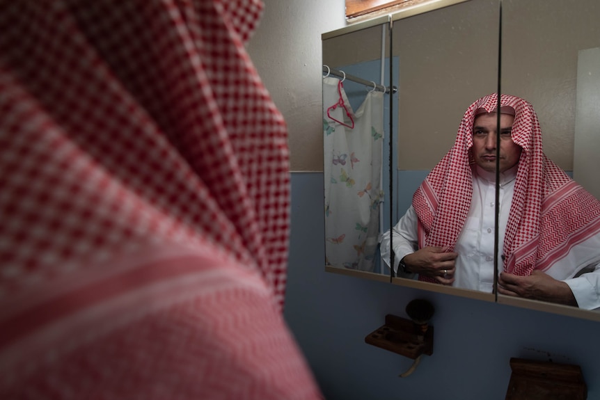 A man in Saudi clothing looking in the mirror.