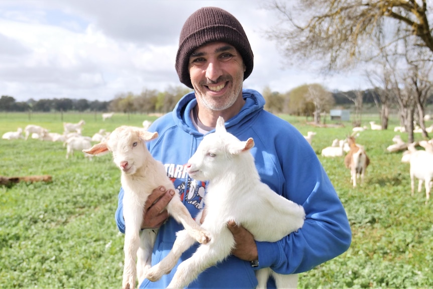 A man holds two new born goats in his arms