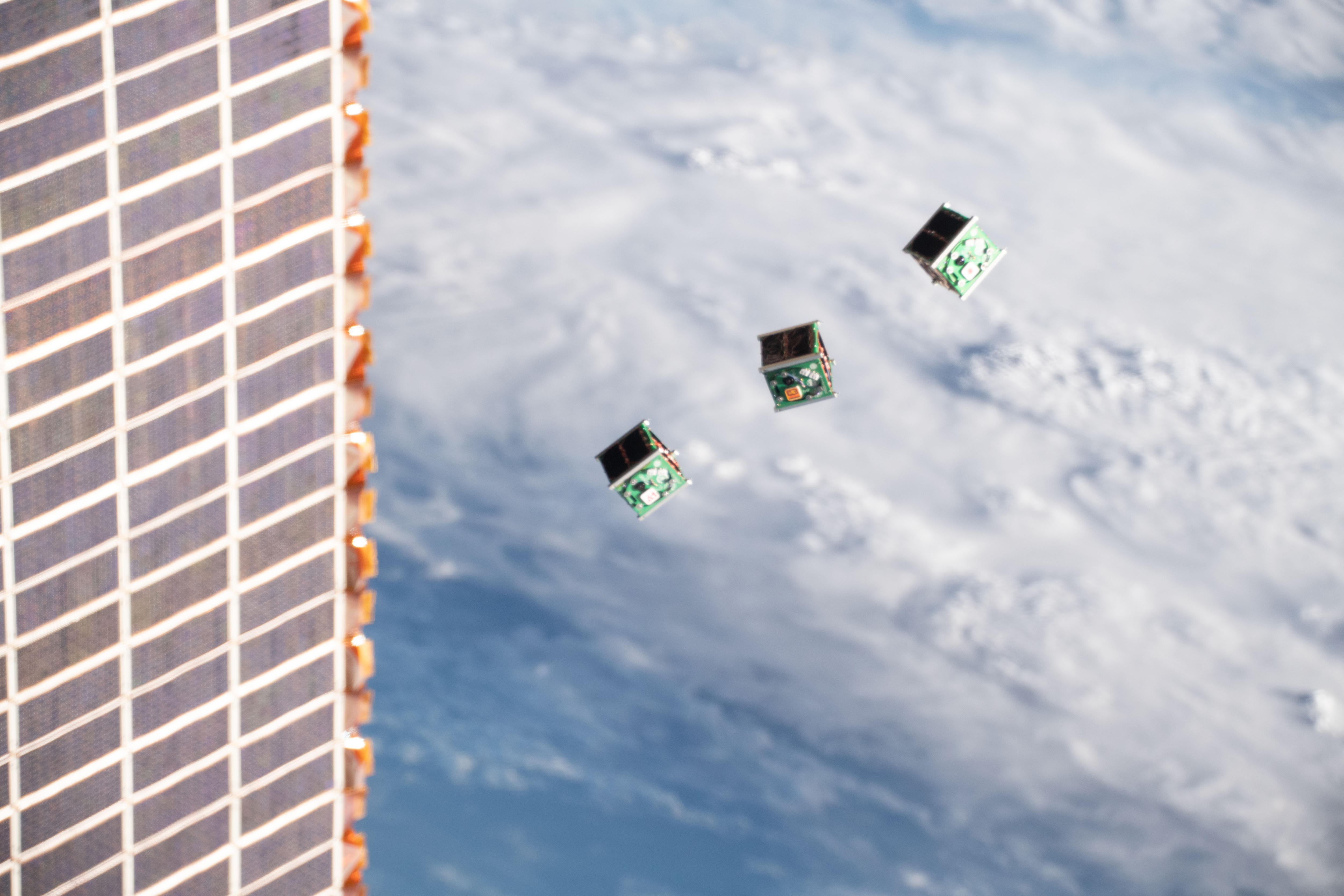 Three small cube-shaped satellites moving away from a launch vehicle in space.