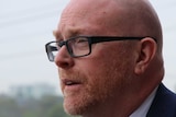 A close-up photograph of John Crowley, a man with black glasses, a bald head and a short red beard.