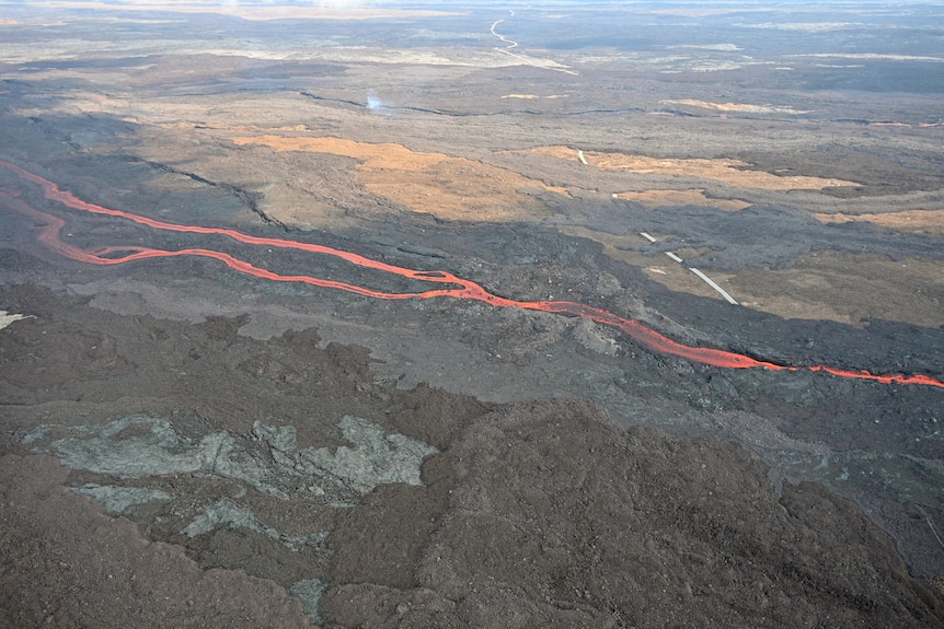 A stream of red glowing lava is pictured from high above, crossing over a road.