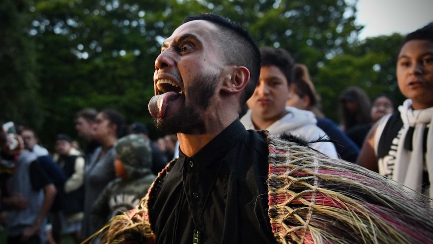 A Maori community leader with wide eyes sticks his tongue out as he performs haka.