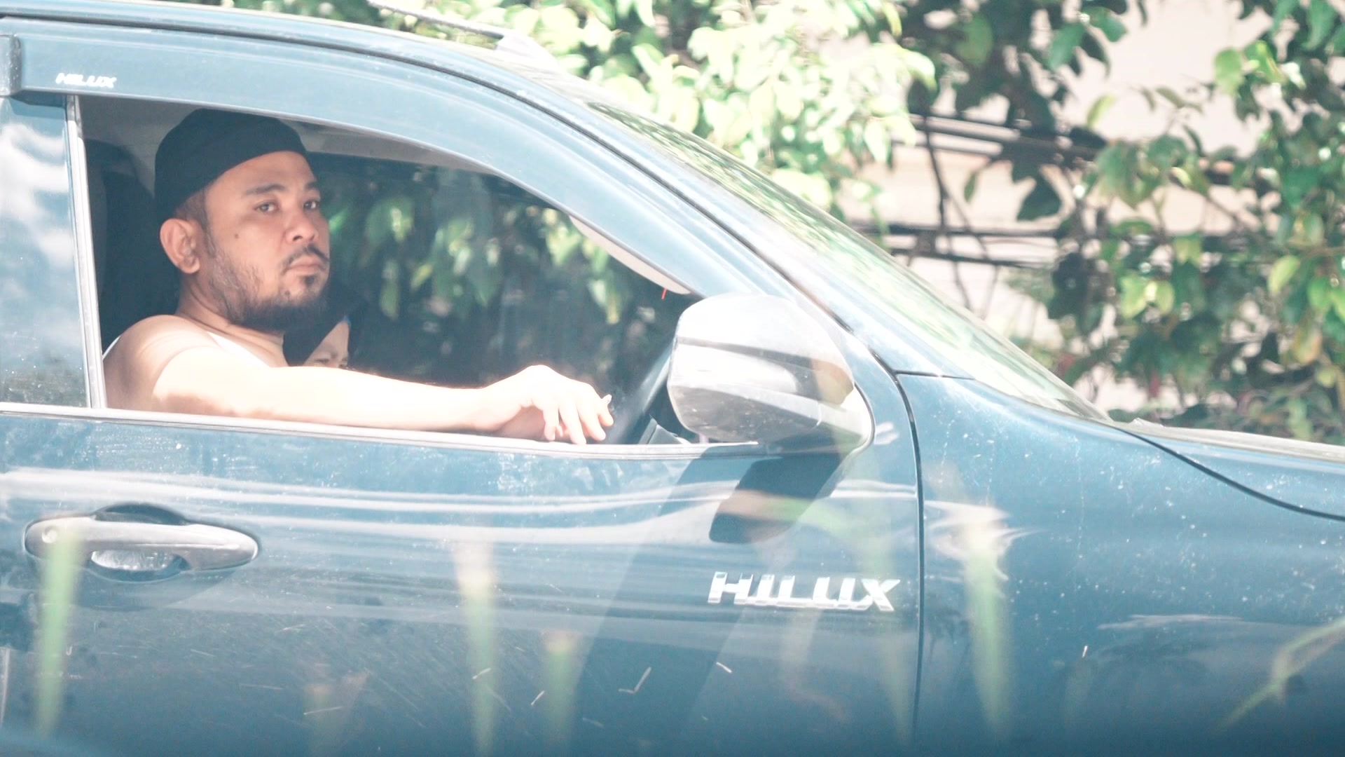 一名男子坐在一辆海拉克斯 (Hilux) 车内，看着驾驶座窗外。 