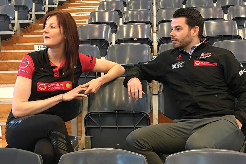 Kate Shimmin and Dan Ryan sit in stadium stand and watch something to their right.