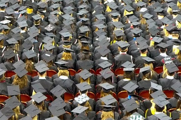 Students wearing mortarboards and gowns seen from above at a university graduation ceremony.