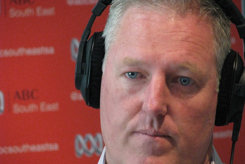 A heasdshot of Troy Bell being interviewed in front of an ABC banner. He is wearing headphones.
