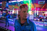 A man looks on, with bright coloured lights behind him