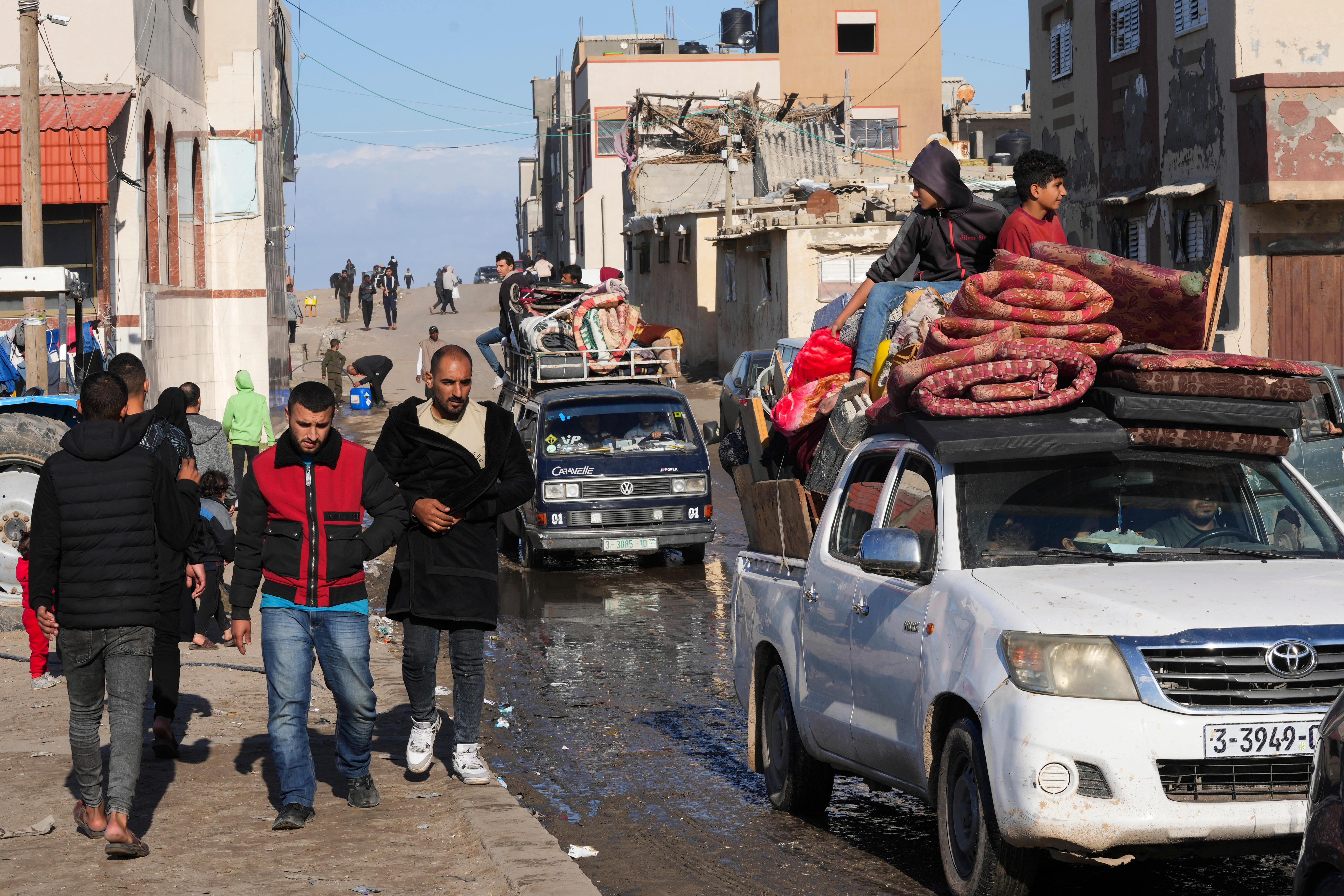 Three men walking beside cars with rugs and other items on their roofs. 