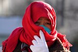 A person in a red scarf adjusts their face mask walking down a street in Beijing.