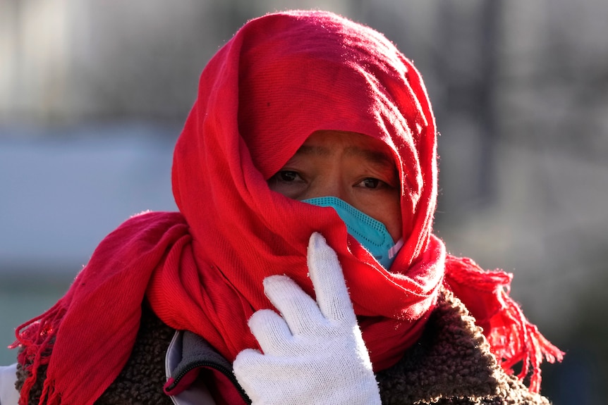 A person in a red scarf adjusts their face mask walking down a street in Beijing.