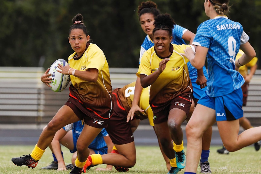 A player runs with the ball with her teammate beside her at a rugby tournament.