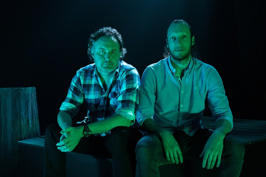 Two men wearing shirts sitting down with a green-blue filter