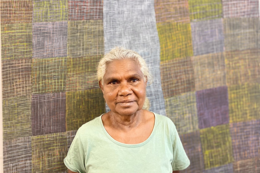 A woman looks into the camera with a painting behind her.