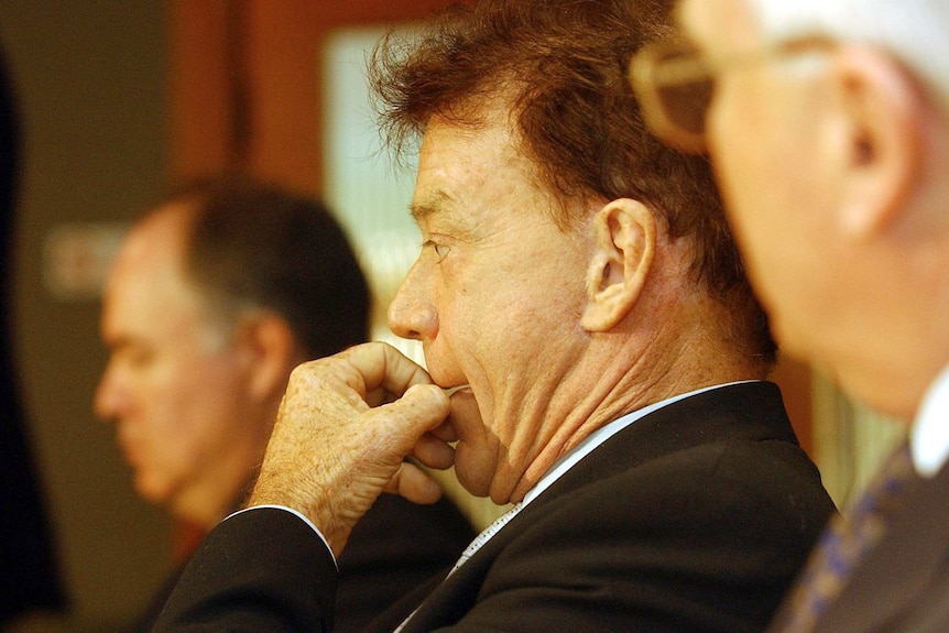 Johnny Warren looks off to the left of the frame, with Les Murray out of focus in the foreground, at right.