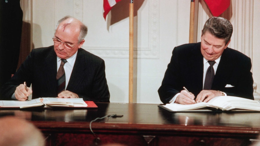 Archival photo of Gorbachev and Regan signing an agreement in front of an American flag in the White House.