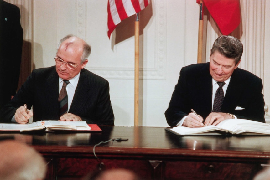 Archival photo of Gorbachev and Regan signing an agreement in front of an American flag in the White House.