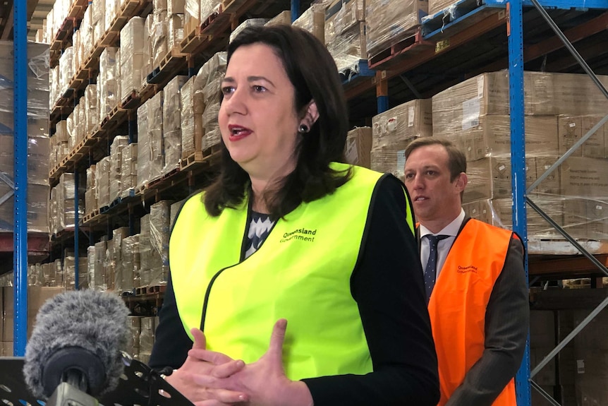 Queensland Premier Annastacia Palaszczuk wears a high-vis vest with walls of boxes behind her.