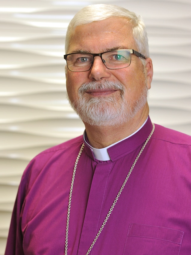 A man in a purple shirt smiles at the camera.