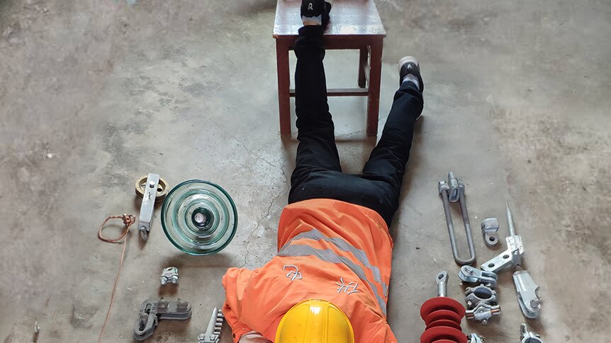 A Chinese factory worker lying on the ground with his tools for work in a factory environment.