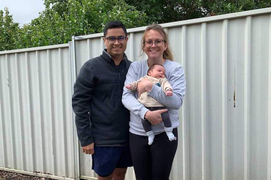 A man and woman with a baby outside a white steel fence.