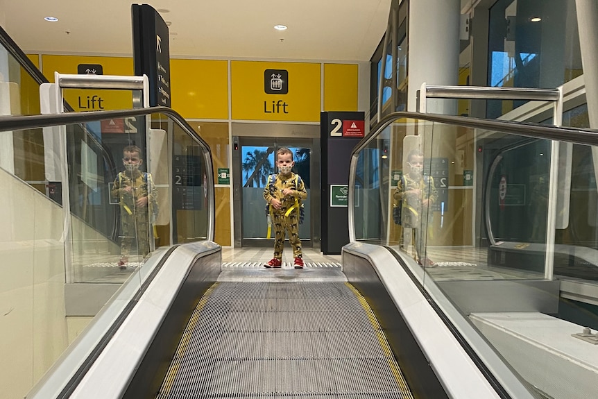 A young boy at the top of an airport escalator.