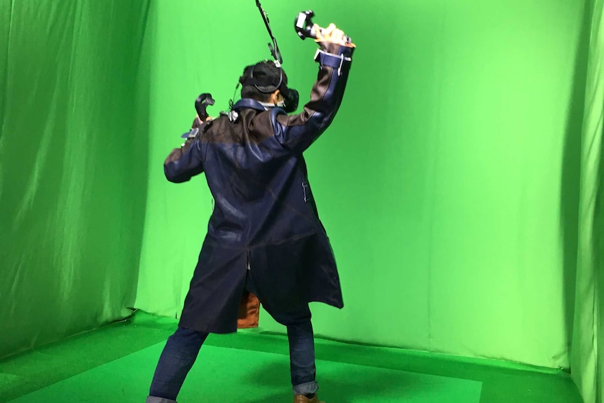 A man stands in front of a green screen holding new technology