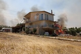 A fire burns near a house surrounded by smoke