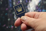 A close-up of a plastic pick with the Crown symbol on it.