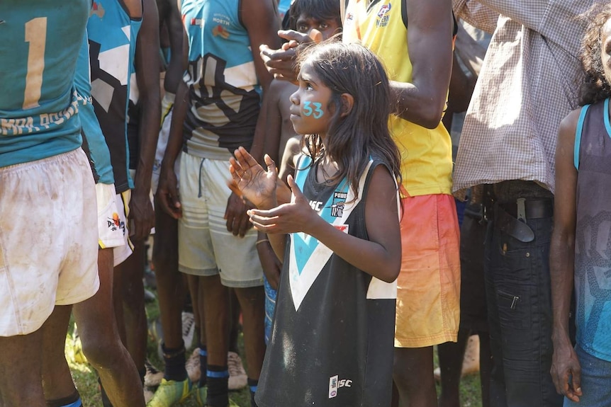 A young Palumpa fan with a 33 written in teal face paint on her cheek watches on as her team takes their final huddle.