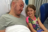 Sian and Matt Downey lying in a hospital bed, smiling at each other.